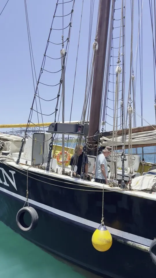 Ide Min lying alongside a quay in turquoise water, crew moving about her deck, a yellow fender hanging against the black hull