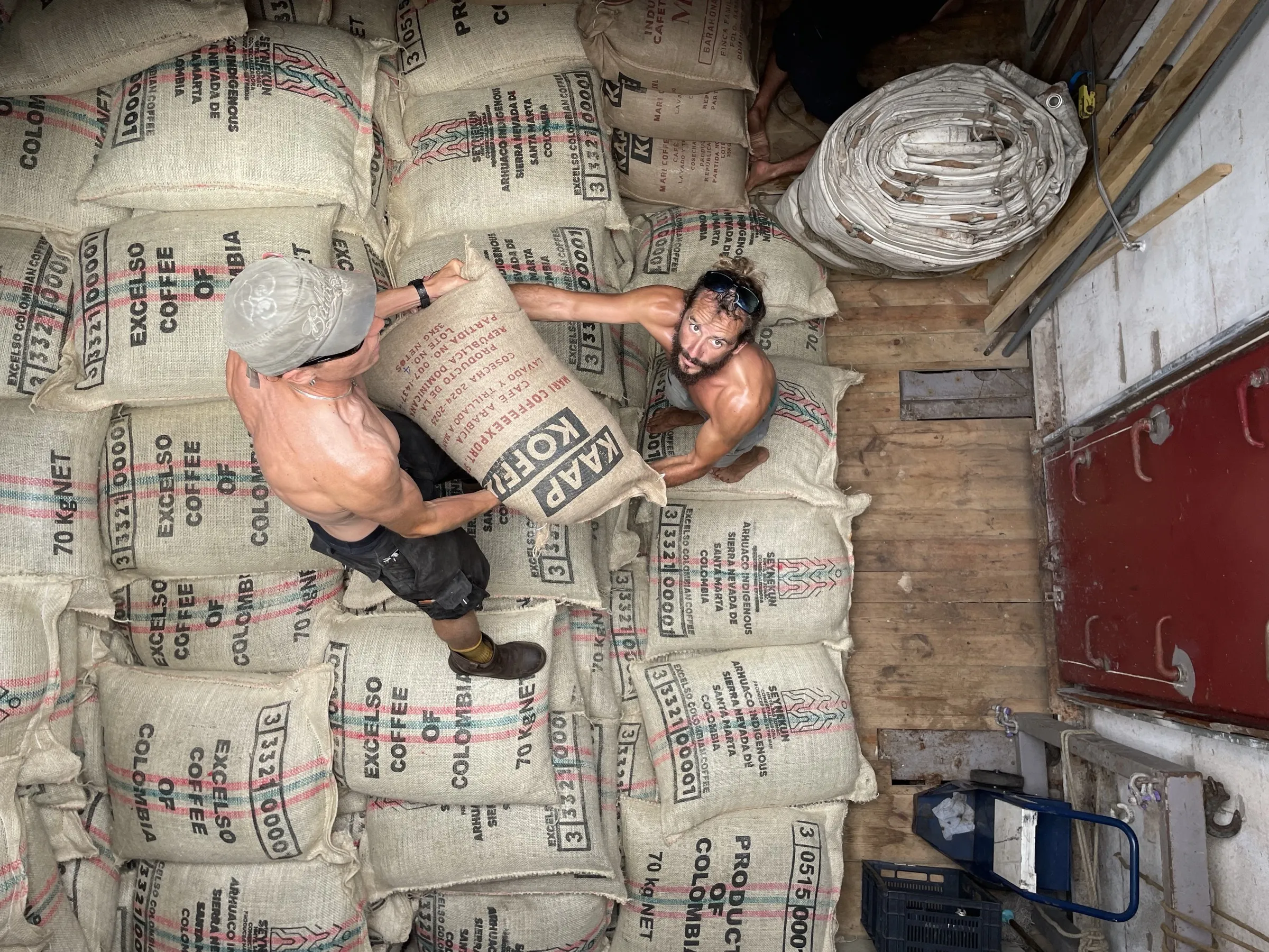 Two crew passing a stamped coffee sack hand to hand overhead in the hold