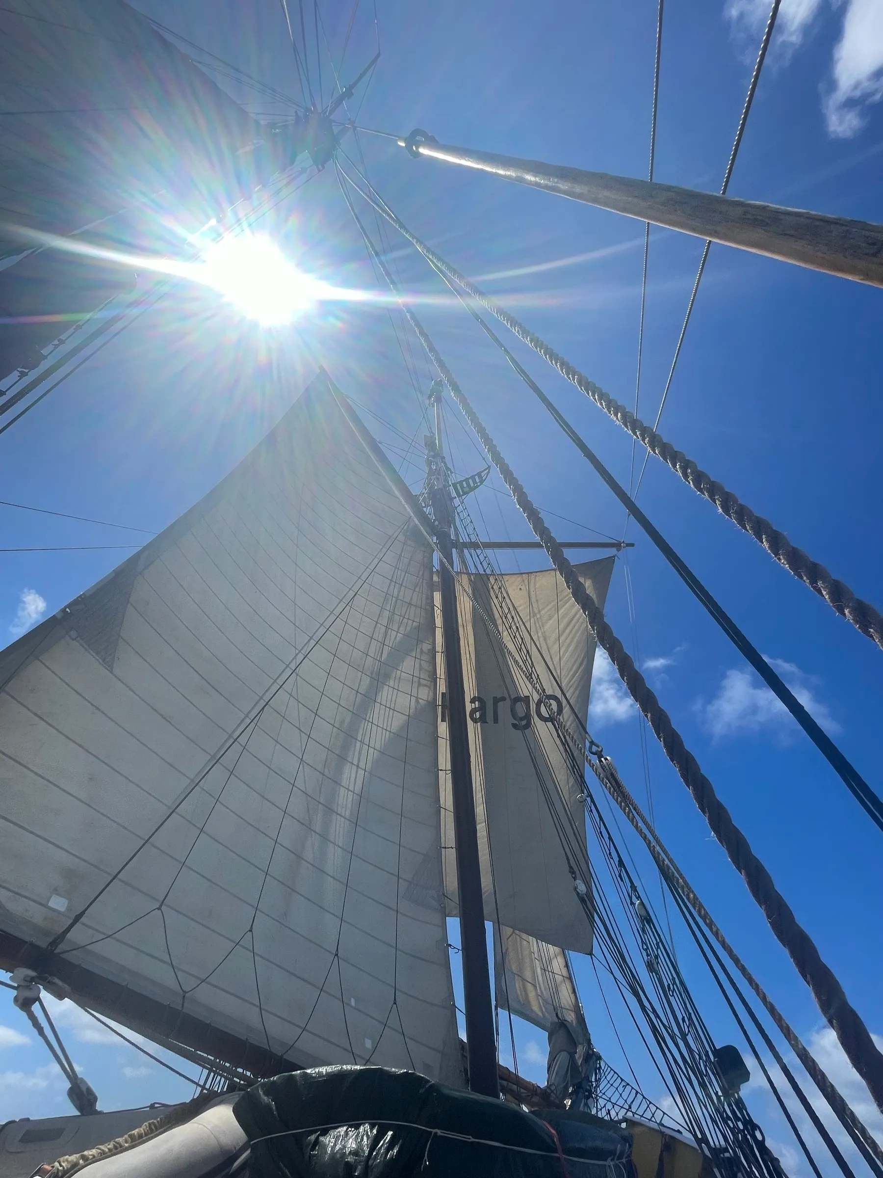 Looking up from the deck at Ide Min's sails drawing full against a blue sky, the sun flaring through the rigging