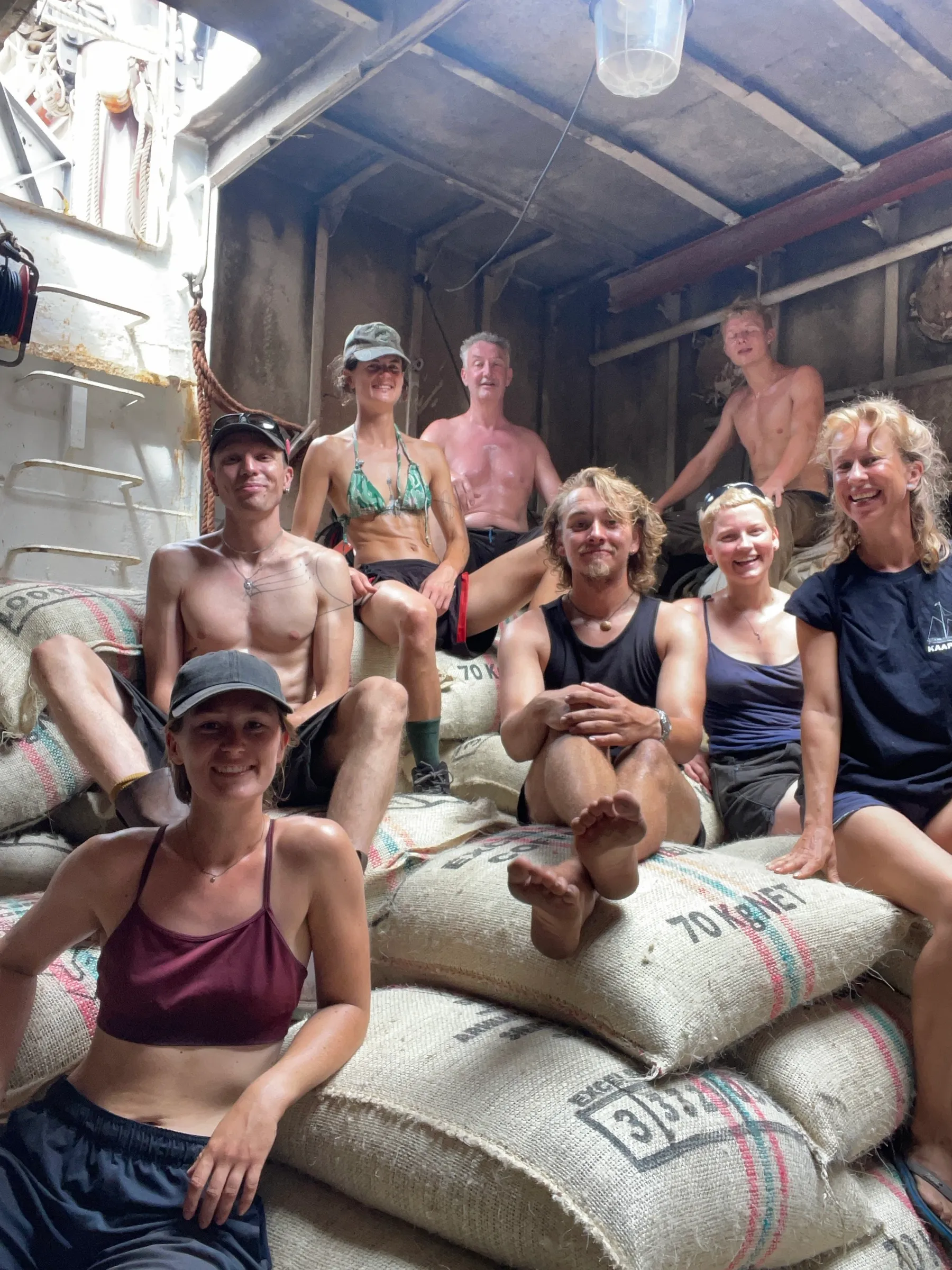 The crew sitting together on stacked coffee sacks below deck, smiling