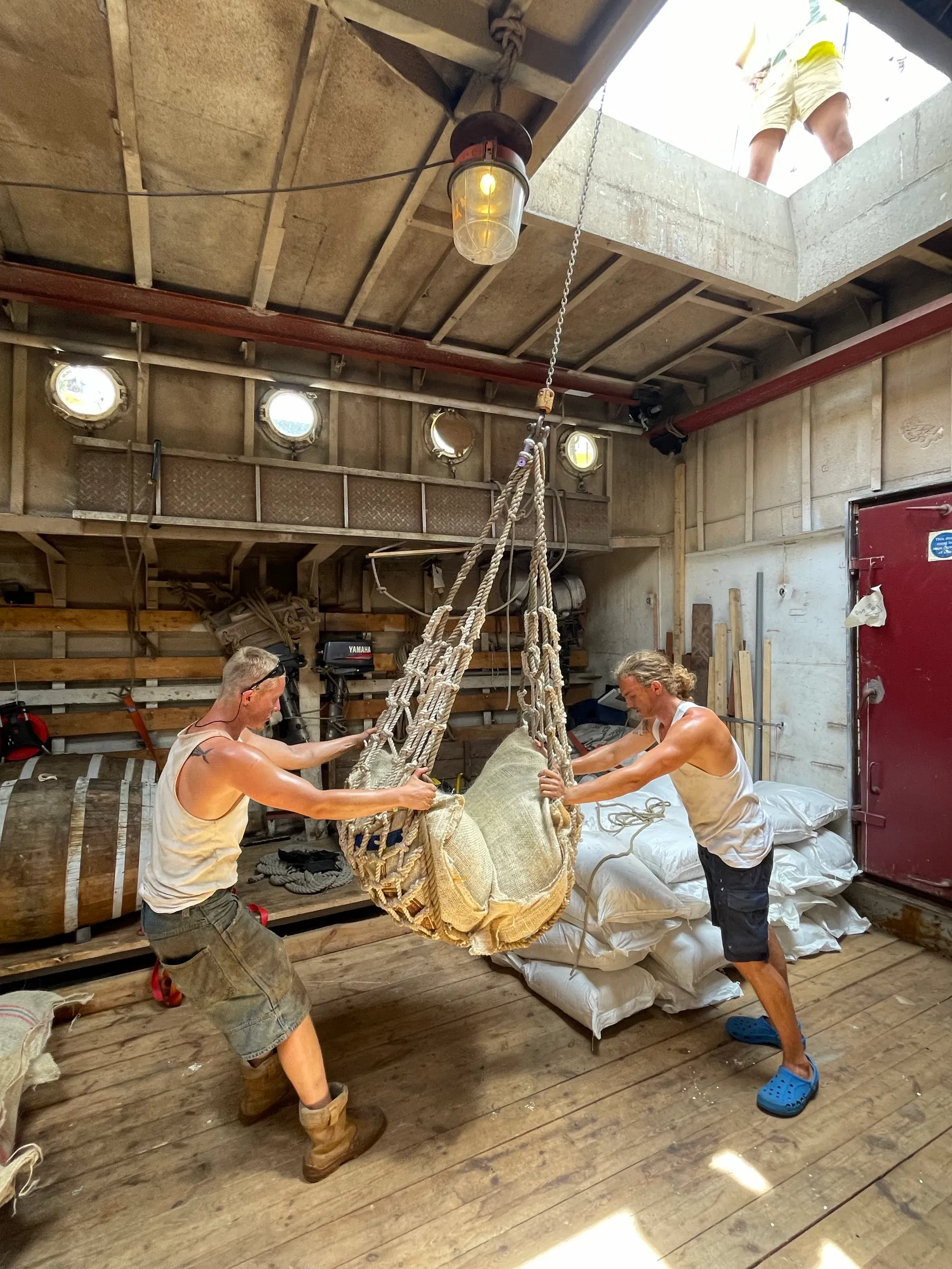 Two crew swinging a cargo net loaded with a sack down into the hold